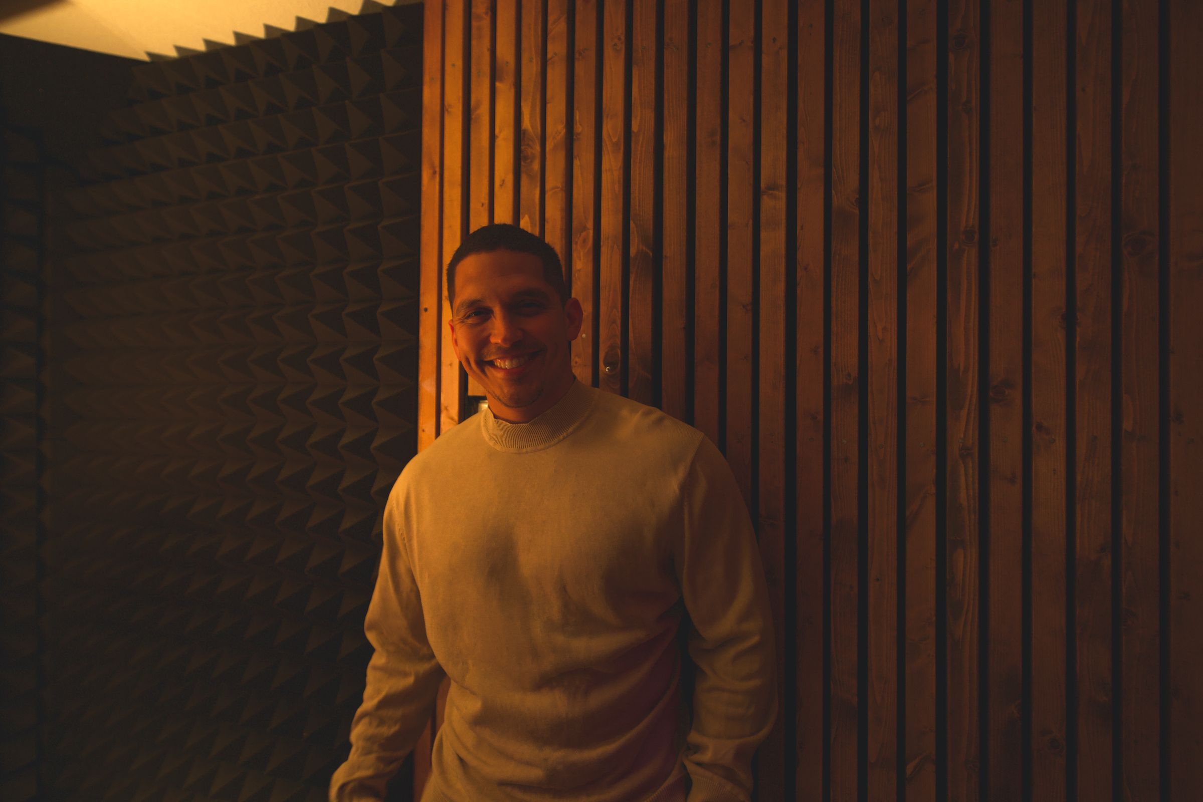 Alex Ruiz smiling in a wood-panelled recording studio